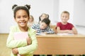 Happy girl keeping books in hands and posing in classroom