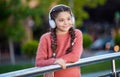 Happy girl listening to audio course outdoors. Teen girl listening to headphones leaning on railing