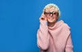 Happy girl listens to music in headphones wearing a sunglasses, knitted hat, sweater over blue background Royalty Free Stock Photo