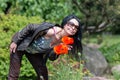 A happy girl with long black hair in glasses sniffing the aroma of large red poppy petals in the garden.