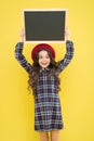 Happy girl with long curly hair in beret. child with empty blackboard. parisian child on yellow. copy space. promotion