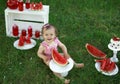 A happy girl looks up at the camera sitting on the lawn with a large piece of sweet juicy watermelon. Royalty Free Stock Photo