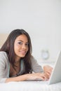 Happy girl lying on bed using her laptop smiling at camera Royalty Free Stock Photo