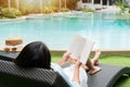 Happy girl lying down on sunbed while reading a book near Swimming Pool on travel holidays vacation, wellness Lifestyle concept. Royalty Free Stock Photo