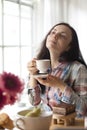 Happy girl with a mug of fragrant coffee in hands. Good breakfast at home in the living room by the window. Free space for text. Royalty Free Stock Photo