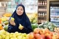 Happy girl in paranja making purchases in supermarket, choosing fresh ripe pears