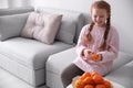 Happy girl peeling ripe tangerine on sofa at home