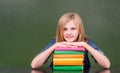 Happy girl with pile books near empty green chalkboard Royalty Free Stock Photo