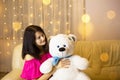 Happy girl in a pink dress hugging a big white soft bear home on the couch. Gift from a loved one, valentine`s day, birthday, Royalty Free Stock Photo