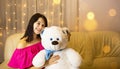 Happy girl in a pink dress hugging a big white soft bear home on the couch. Gift from a loved one, valentine`s day, birthday, Royalty Free Stock Photo