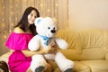 Happy girl in a pink dress hugging a big white soft bear home on the couch. Gift from a loved one, valentine`s day, birthday, Royalty Free Stock Photo