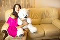 Happy girl in a pink dress hugging a big white soft bear home on the couch. Gift from a loved one, valentine`s day, birthday, Royalty Free Stock Photo