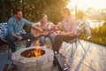 Happy girl playing guitar outdoors by the fireplace, sitting with mother and father in the backyard enjoying sunny summer day Royalty Free Stock Photo