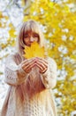 Happy girl playing with leaf, looking at camera and smilling. Autumn portrait woman hides her face yellow maple leaf Royalty Free Stock Photo