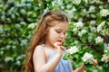 A happy girl is playing under a blooming apple tree with white flowers. A child holds a white flower in his hands.. Summer fun for Royalty Free Stock Photo