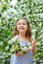 A happy girl is playing under a blooming apple tree with white flowers. A child holds a white flower in his hands.. Summer fun for Royalty Free Stock Photo