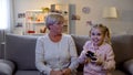 Happy girl playing video game, upset granny enviously looking at granddaughter Royalty Free Stock Photo