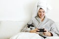 Happy girl playing video games with cat in bed. Beautiful young woman in bathrobe relaxing and lying in bed , hugging cat and