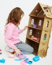 Happy girl plays with doll house and doll house furniture. Funny lovely child is having fun. Royalty Free Stock Photo