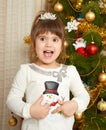 Happy girl portrait in christmas decoration, playing with snowman toy, winter holiday concept, decorated fir tree and gifts Royalty Free Stock Photo