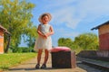 Happy girl on a railway station, waiting for the train with vintage suitcase. Traveling, holiday and chilhood concept. Travel insu