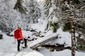 A happy girl, with a red jacket and a red backpack, crossing a wooden bridge, during a winter hiking trip