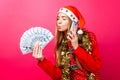 Happy girl in red sweater and Santa hat talking on phone and holding money in hand trying to kiss them, on red background. Royalty Free Stock Photo