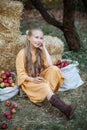 Happy girl in retro yellow dress sits with apples in autumn garden. Royalty Free Stock Photo