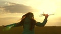 Happy girl runs with a toy airplane on a field in the sunset light. children play toy airplane. teenager dreams of