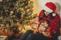 happy girl in santa hat holding gift box at golden beautiful christmas tree with lights and presents in festive room. happy Royalty Free Stock Photo