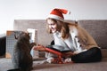 Happy girl in santa hat opening christmas gift box and playing with cat Royalty Free Stock Photo