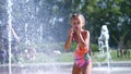 Happy girl of seven years, in swimsuit, having fun between water splashes in fountain . Sunny summer day in the city