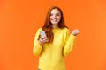 Happy girl share good news with you. Cheerful pretty redhead female holding smartphone, fist pump in triumph or Royalty Free Stock Photo