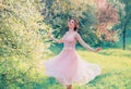 Happy girl in short flying gentle pink dress laughs joyfully, doll princess whirls in bright yellow spring garden with