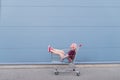 Happy girl sits in a cart for shopping on the background of a blue wall. Street fashion Royalty Free Stock Photo