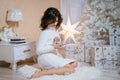 Happy girl sits on floor near festive christmas tree, holds silver christmas Royalty Free Stock Photo