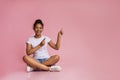 Happy girl sitting with crossed legs and pointing fingers upwards Royalty Free Stock Photo