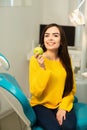 Happy girl sitting in dental chair and showing fresh apples after successful dental treatment