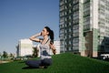 A happy girl is sitting on the green grass and listening to music in the courtyard of her house. Beautiful territory of a Royalty Free Stock Photo