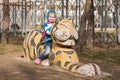 Happy girl sitting on a sculpture of a tiger on playground in Anapa