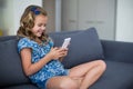 Happy girl sitting on sofa and using mobile phone in living room Royalty Free Stock Photo