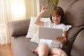 Happy girl sitting on sofa waving funny on tablet