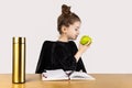 A happy girl sitting at a table reading a book and eating an apple Royalty Free Stock Photo