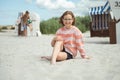 Happy girl sitting on white beach and brother on backround playing with ball at summer holidays Royalty Free Stock Photo