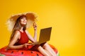 Happy girl in straw sits in inflatable ring works on laptop on yellow background. freelancer. Travel