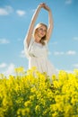 Happy girl stretch oneself in rape seed flowers field posing in white dress Royalty Free Stock Photo