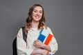 Happy girl student holding backpack, book, notebook, passport isolated on a dark grey background, copy space, immigration,