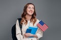 Happy girl student holding backpack, book, notebook, passport and USA flag isolated on a dark grey background