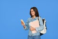 Happy girl student holding backpack using mobile cell phone isolated on blue. Royalty Free Stock Photo