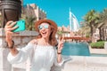 Happy girl takes a photo on her smartphone against the backdrop of the cityscape in Dubai with the hotel Burj al Arab Royalty Free Stock Photo